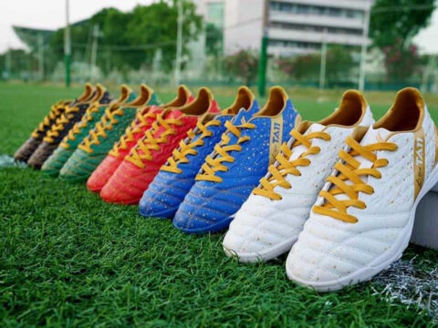 Hàng giày đá bóng sân cỏ nhân tạo nhiều màu sắc dây vàng xếp trên mặt cỏ